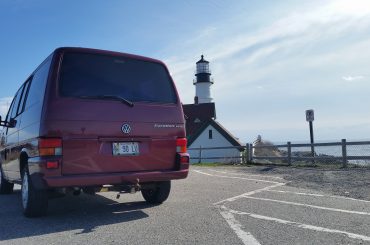 A burgundy Volkswagen van in front of a lighthouse.
