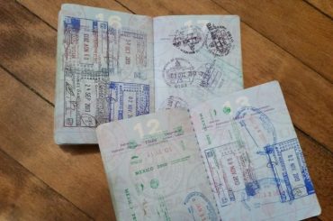 Two passports on a wooden floor, both opened and showing many stamped pages.