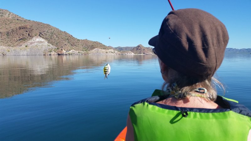 A woman with a green life vest catching a small fish off the coast of Baja California.