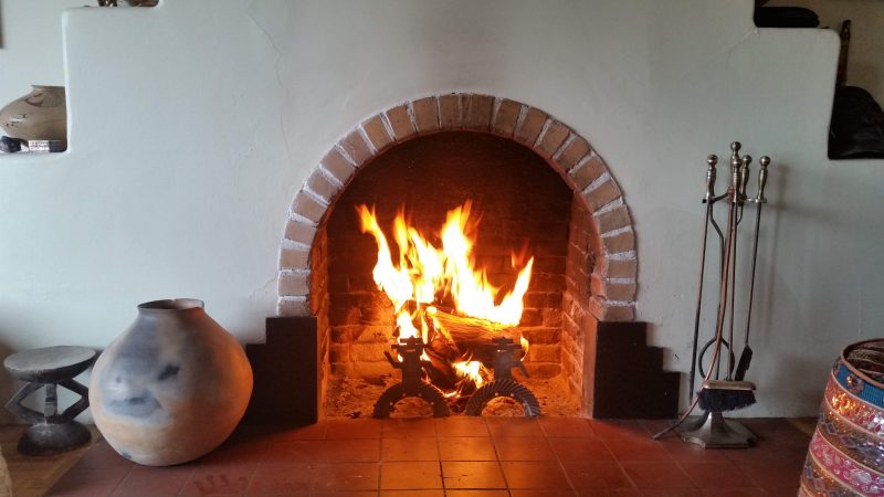 An adobe fireplace with a blazing fire inside of it.