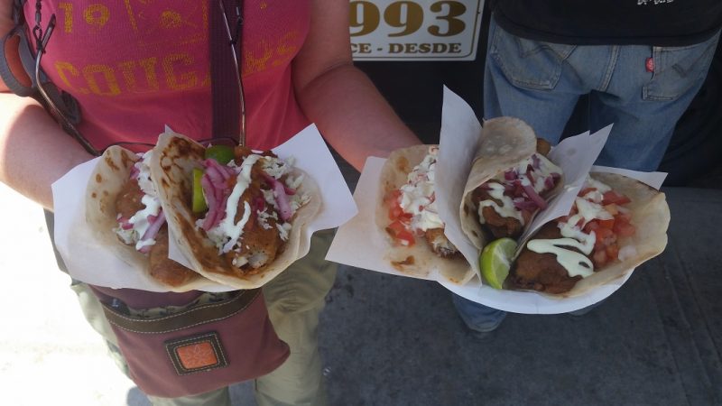A woman holding two plates, each with two fish tacos topped with slaw, mayonnaise and red onions.