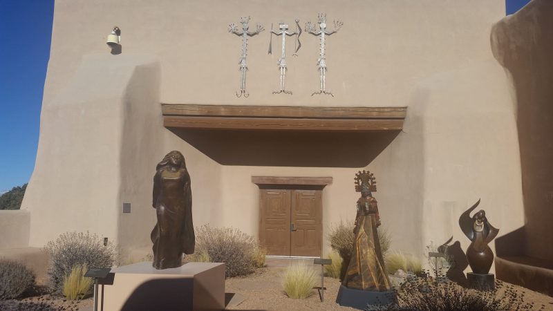 Three bronze statues in front of an adobe building.