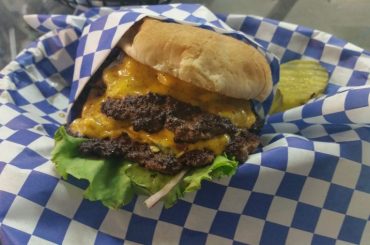 a burger basket containing the best green chile cheeseburger in Albuquerque, with a pickle on the side.