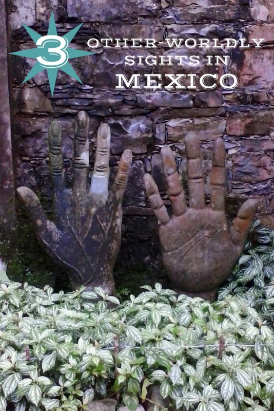 Two concrete statues of right hands in a bed of green plants.