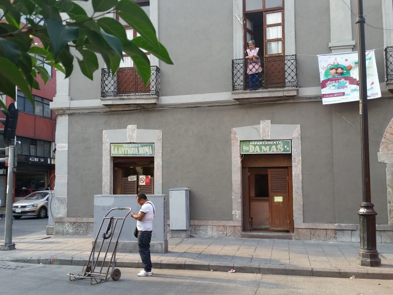A woman standing on a balcony looking down on the street at a man with a cart.