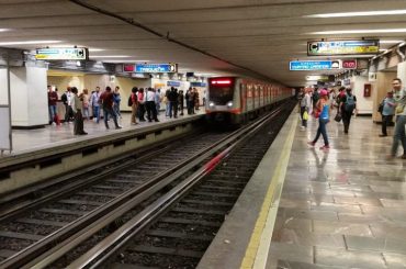 People standing on a platform of a subway station in Mexico City as a train is pulling in.