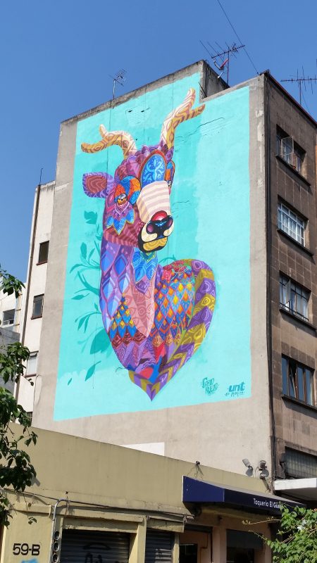 The side of an apartment building in Mexico City painted with a very colorful image of a male deer.