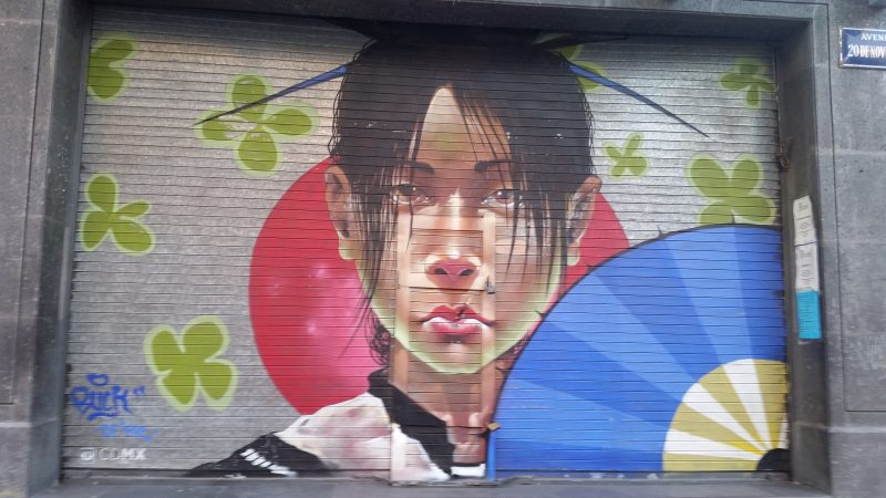 An image of urban artwork depicting a woman with a blue folding fan.