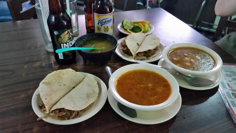 Two bowls of soup and a plate of two tacos with several bottles of beer, served as botanas in a cantina in Mexico City.