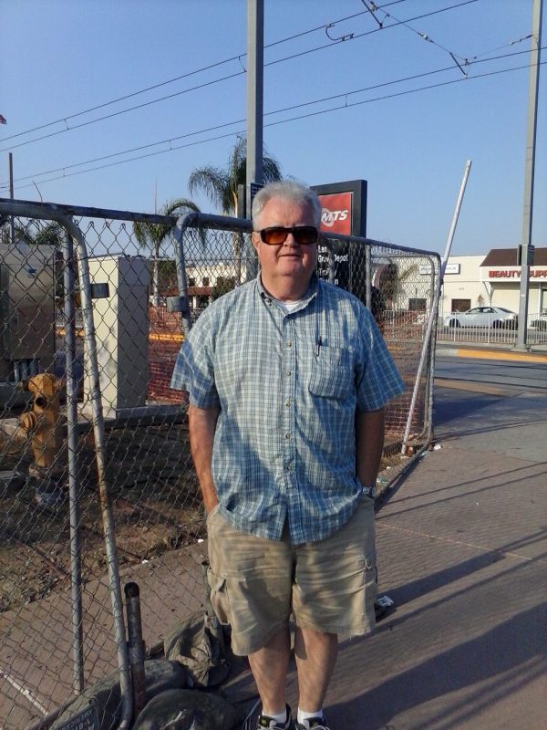Man with sunglasses in front of a chain link fence.