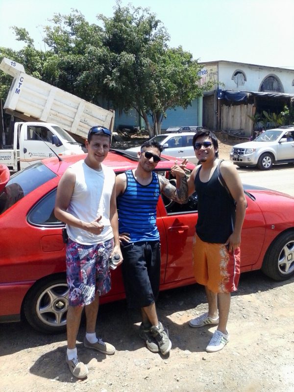 Three men in front of a red car.