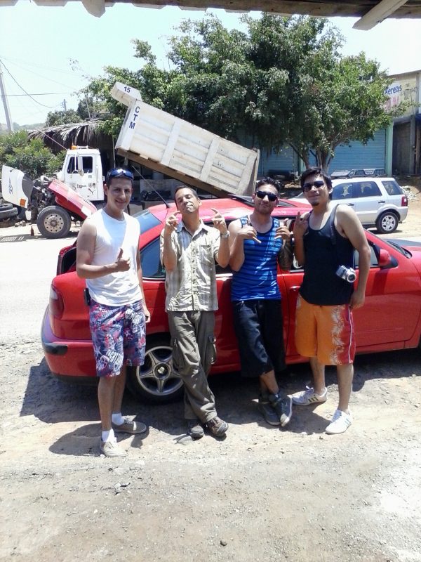 Four men in front of a red car.