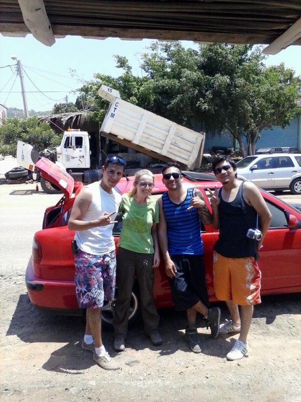 Three men and a woman in front of a red car.