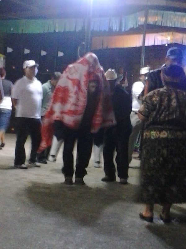 A man giving a piggy-back ride to San Simon, who has a blanket draped over him, in Zunil, Guatemala.