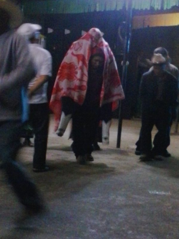 A man giving a piggy-back ride to San Simon, who has a blanket draped over him, in Zunil, Guatemala.