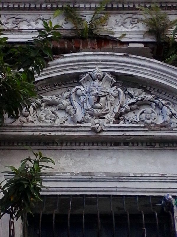 A cracked facade of a colonial building with vegetation sprouting from it in San Salvador, El Salvador.