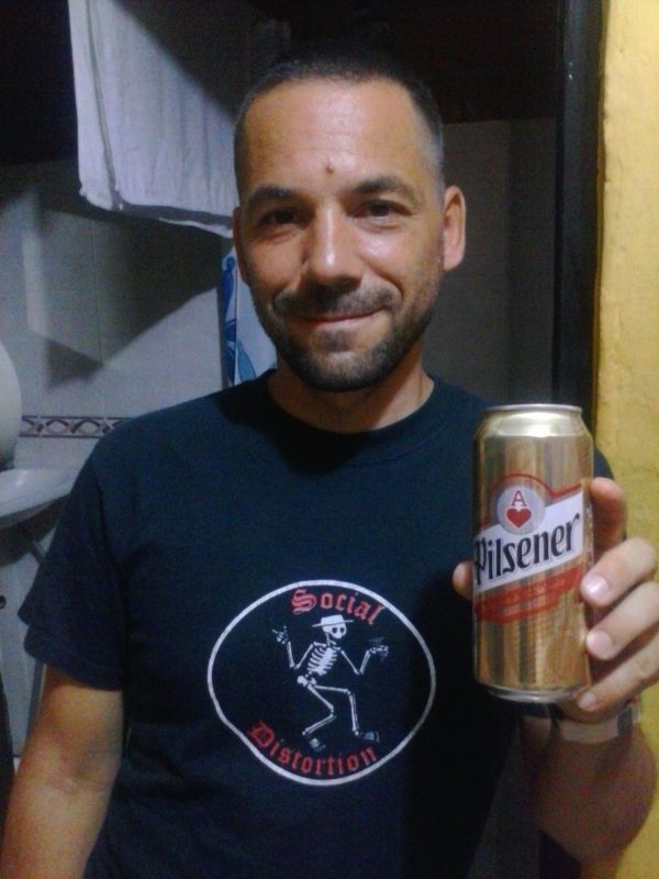 man in black shirt holding a gold can of Pilsner beer in El Salvador.
