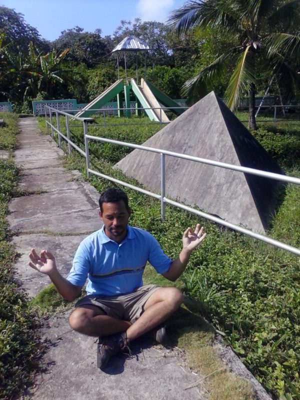 A man doing a yoga pose in front of a concrete pyramid.
