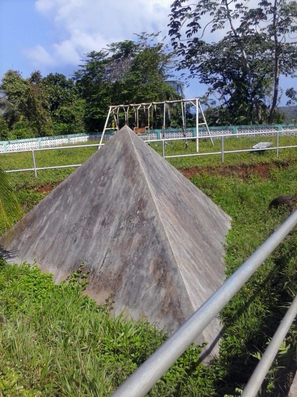 A concrete pyramid with a playground swing in the background.