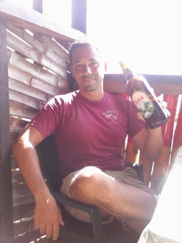 Man in burgundy shirt holding a bottle of Tona beer on Big Corn Island off the coast of Nicaragua.