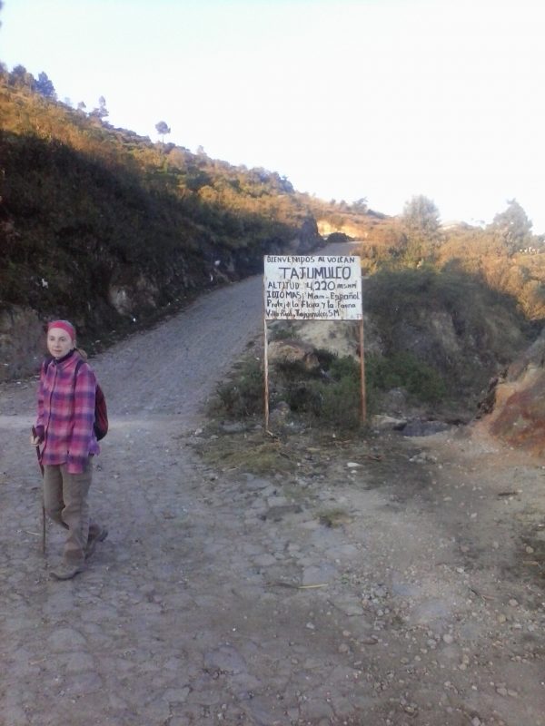 A woman in a pink jacket standing in front of Volcan Tajumulco trailhead