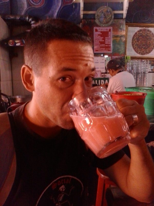 A man drinking a mug of pink pulque.