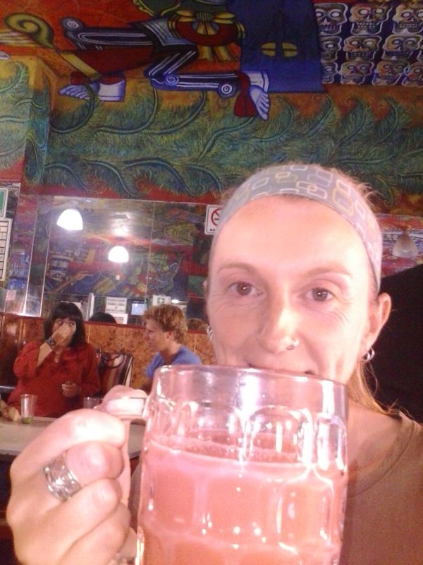 A woman drinking a mug of pink pulque.