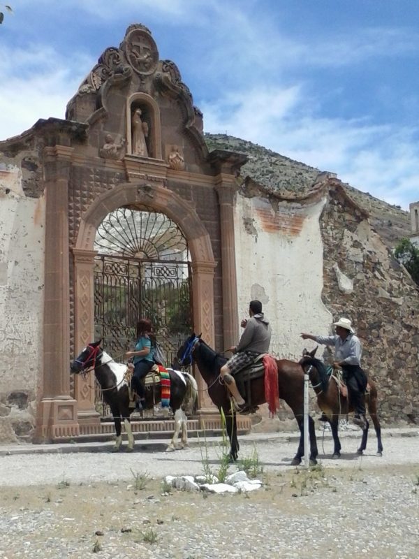 Three people on horseback in front of an old church gate in the town of real de Catorce in San Luis Potosi state in Mexico.