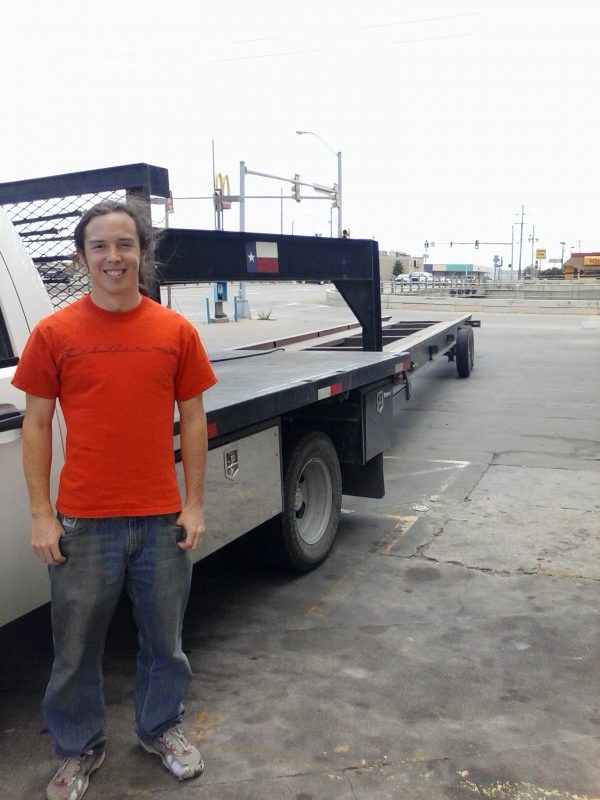 Man in orange shirt posing for a photo next to a trailer.