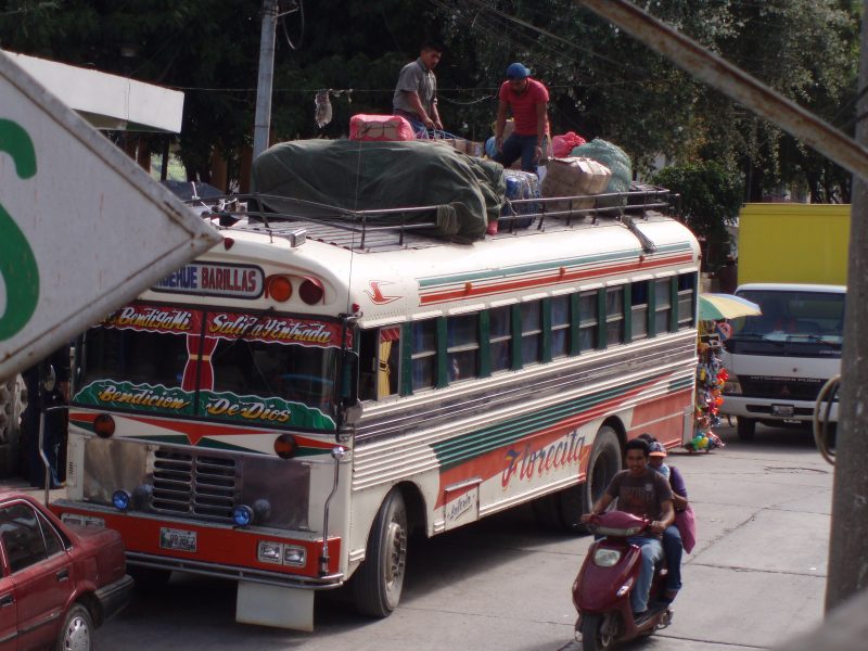 Two men tying down cargo on the top of a brightly-colored chicken bus in Guatemala.