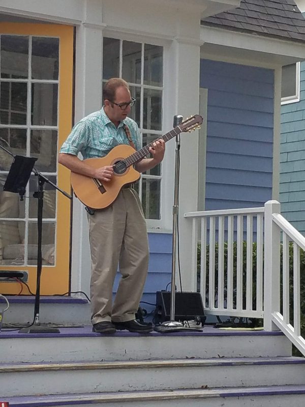Sean Mencher playing an acoustic guitar at a Porchefest event held annually on a summer weekend in Portland, Maine.