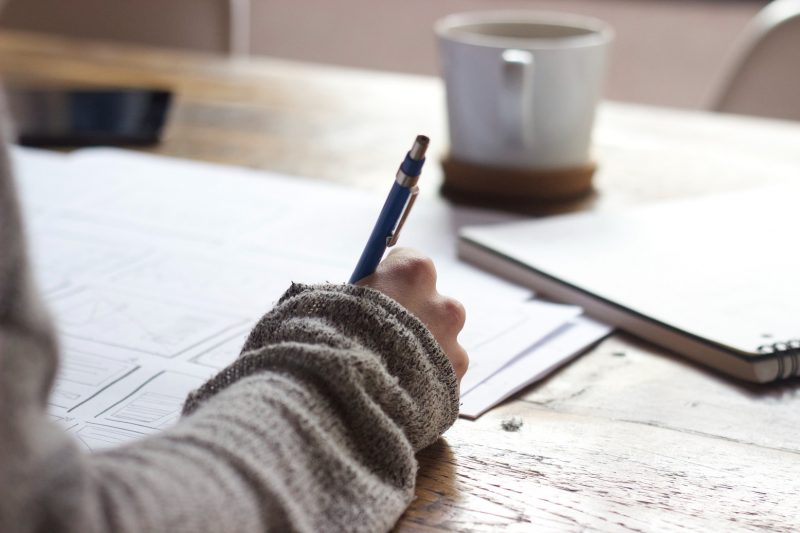 A person sitting down at a desk writing down travel blog name ideas on a piece of paper.