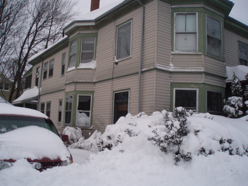 A large amount of snow covering a van and some shrubs in front of a house in Portland, Maine.